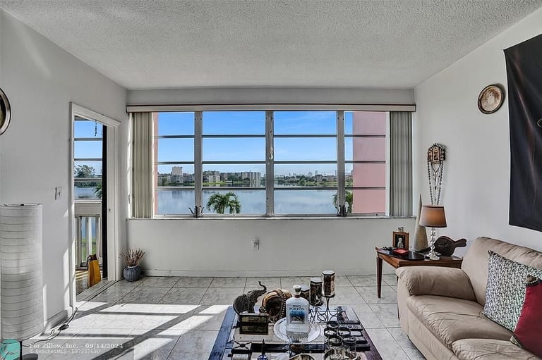 Modern living room with floor-to-ceiling windows overlooking a river, furnished sofa, glass coffee table, and natural lighting